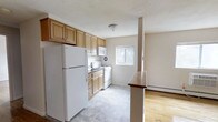 Located at 221 South Oak Avenue in Clifton Heights, Pennsylvania, this single-floor space offers a functional and well-organized layout designed for comfortable everyday living. The kitchen serves as a central feature, outfitted with warm-toned wood cabinetry that provides generous storage both above and below the countertops. White appliances, including a full-size refrigerator, electric range, and microwave, are neatly integrated into the layout. A window above the sink allows natural light to brighten the cooking area, enhancing the overall sense of openness. The kitchen flows directly into an adjoining living area, separated by a partial partition with a wood-finished countertop ledge that adds both visual definition and functional surface space. The living area features classic hardwood flooring, adding warmth and a timeless quality to the space. Light, neutral wall tones throughout contribute to an airy, cohesive atmosphere. A baseboard heating unit is visible along the wall, ensuring year-round comfort. The seamless transition between the kitchen and living areas creates an open, connected feel that makes the space practical and inviting.