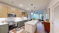 Located in the heart of downtown Raleigh at 222 N West St, this well-appointed one-bedroom, one-bathroom residence offers a thoughtfully designed single-floor layout with modern finishes throughout. Light wood-tone flooring flows seamlessly across the open-concept living and kitchen areas, creating a warm, cohesive aesthetic.

The kitchen is a standout feature, showcasing two-tone cabinetry with sage green lower cabinets and natural wood upper cabinets paired with open shelving. A large white waterfall island anchors the space, illuminated by stylish globe pendant lights. Stainless steel appliances, white subway tile backsplash, and recessed lighting complete the contemporary look.

The living room benefits from multiple windows that invite abundant natural light and offer urban city views. The space feels open and airy, with clean white walls that complement the warm flooring.

The bedroom is distinguished by rich teal accent walls, large windows with city views, and a ceiling fan. Two closets provide ample storage.

The bathroom features a long vanity with sage green cabinetry, a backlit mirror, and a full tub-shower combination with white subway tile. Additional conveniences include in-unit laundry and a utility room, making this a fully functional and stylish downtown residence.