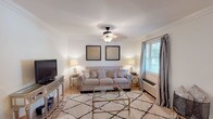 This single-story, 2-bedroom, 1-bathroom residence in Baton Rouge, Louisiana offers a thoughtfully arranged floor plan with distinct living, dining, and kitchen areas. The living room serves as the central gathering space, featuring crown molding, a ceiling fan with light fixture, and a large window dressed with gray curtains that allow natural light to filter in. The room's neutral palette and warm hardwood-style flooring contribute to its inviting atmosphere.

Adjacent to the living room, the dining area accommodates a round table for four beneath a classic pendant light fixture, with its own window enhancing the bright, open feel. The galley-style kitchen is efficiently designed, offering rich cherry cabinetry, dark granite countertops, tile flooring, and stainless steel appliances including a range, microwave, refrigerator, and dishwasher.

Both bedrooms feature carpeted floors, ceiling fans, and windows with natural light. The shared full bathroom includes a tub/shower combination, a vanity with granite countertops, matching cherry cabinetry, and tile flooring, maintaining consistent finishes throughout the home.