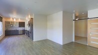 This single-floor space showcases a clean, modern design with an open-concept layout that connects the living area to the kitchen. The flooring throughout is a warm-toned, wood-look laminate that adds continuity and a contemporary feel to the space. Neutral, light-colored walls create a bright and airy atmosphere, complementing the overall aesthetic.

The kitchen is outfitted with dark, espresso-toned cabinetry that provides a striking contrast against the stainless steel appliances, including a full-size refrigerator. The cabinetry extends along the wall, offering ample storage, while the countertops and fixtures contribute to the kitchen's polished, functional design.

A partial wall partially divides the open living space, adding subtle architectural definition without compromising the open feel. On the opposite side of the living area, a barn-style sliding door is visible, adding a stylish, industrial touch to the space. Recessed and flush-mount ceiling fixtures provide consistent, practical lighting throughout. The overall design is cohesive, modern, and well-suited for everyday living.
