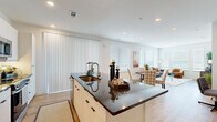 This thoughtfully designed 2-bedroom, 3-bathroom single-floor residence offers a seamless open-concept layout that connects the kitchen, dining, and living areas into one cohesive, light-filled space. The modern kitchen is a standout feature, showcasing crisp white cabinetry that extends to the ceiling, stainless steel appliances, and a large central island topped with dark granite countertops that doubles as a breakfast bar with leather-upholstered stools. The open dining area flows naturally into the bright living room, where light wood-look flooring, large windows with horizontal blinds, and a sliding door with vertical blinds invite abundant natural light throughout the day. The primary bedroom is a serene retreat, carpeted for comfort and fitted with a ceiling fan, multiple windows, and access to a dedicated closet with full rod-and-shelf storage systems. The second bedroom mirrors this warmth with carpet flooring, generous natural light, and its own ceiling fan. The bathrooms feature elegant tile work, including a shower with floor-to-ceiling linear stone-look tile and a glass enclosure. Two well-organized closets provide ample storage throughout the residence, completing this functional and contemporary living space.