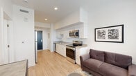 Located at 335 Victoria St in Colorado Springs, Colorado, this efficiently designed one-bedroom, two-bathroom unit offers a thoughtful layout that maximizes every square foot. The open-plan living and kitchen area anchors the space, featuring light wood-style flooring that runs throughout, crisp white walls, and recessed lighting that keeps the atmosphere bright and clean. The kitchen is well-equipped with stainless steel appliances — including a range, microwave, dishwasher, and refrigerator — complemented by white cabinetry, sleek bar-pull hardware, and neutral countertops. The living area flows naturally from the kitchen, with a window at the far end drawing in natural light. A connecting hallway leads to the private bedroom, a cozy retreat with plush carpet, a large window fitted with blinds, and generous closet storage behind paneled double doors. The two bathrooms are finished in a clean, contemporary style, with one featuring a soaking tub with chrome fixtures and a white vanity with ample storage. The overall design is modern and cohesive, with a neutral palette and functional finishes that create a comfortable, move-in-ready environment suited to everyday urban living in downtown Colorado Springs.