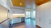 Located at 1090 NE 91st Ave in Hillsboro, Oregon, this thoughtfully designed single-floor residence blends modern finishes with warm architectural details throughout. A standout feature of the space is the natural wood-paneled ceiling that spans the kitchen and living areas, adding warmth and texture to the otherwise clean, contemporary aesthetic.

The kitchen is well-appointed with white flat-front cabinetry, light countertops, a white subway tile backsplash with under-cabinet lighting, and a full suite of stainless steel appliances including a range, over-the-range microwave, dishwasher, and refrigerator. Wood-toned luxury vinyl plank flooring ties the kitchen seamlessly into the open living area, which is brightened by large windows and French doors that open onto a private balcony offering views of the surrounding neighborhood.

The bedrooms feature plush carpeting, ceiling fans, natural wood ceilings, and generous windows that invite abundant natural light. The bathrooms are clean and functional — one featuring a undermount sink with light quartz countertops and a tub-shower combination, while the second offers built-in shelving, wood-look flooring, and a shower-tub combo. Ceiling fans throughout the unit enhance comfort and airflow. The overall ambiance is bright, modern, and welcoming.
