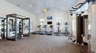 Located in Hilliard, Ohio, this single-floor fitness center at 2640 Lakebridge Ln is a thoughtfully designed community amenity space built to accommodate a full range of workout needs. The facility is defined by its soaring vaulted ceilings, which lend an open, airy feel throughout the main workout area, and recessed lighting that keeps the space bright and energizing at any time of day.

The main exercise floor is finished with durable, textured carpet tiles and features an impressive array of equipment, including multiple treadmills and elliptical machines positioned along a wall of windows that flood the area with natural light. Wall-mounted flat-screen televisions are conveniently placed for viewing during cardio sessions. A large floor-to-ceiling mirror along one wall visually expands the space while supporting strength and form training.

The strength zone is well-appointed with a multi-functional cable and weight rack system, a full dumbbell rack, a workout bench, stability balls, and medicine balls, offering versatility for users of all fitness levels. A water dispenser and built-in cabinetry provide practical convenience. The entryway area transitions seamlessly from the exterior, featuring hardwood-style flooring, a seating bench, and glass panel doors that bring in additional natural light, creating a welcoming arrival experience into the fitness center.