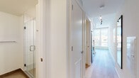 This thoughtfully designed single-floor unit offers a clean, contemporary aesthetic throughout. Light wood flooring runs seamlessly across the open-plan living space, creating a warm and cohesive feel. The compact yet highly functional kitchen is outfitted with stainless steel appliances, including an induction cooktop, built-in oven, microwave, and refrigerator, complemented by crisp white cabinetry, a stainless steel sink with a chrome pull-down faucet, and a distinctive white hexagonal tile backsplash that adds subtle texture to the minimalist design.

The living and sleeping area is cleverly integrated through a partial dividing wall that incorporates a pass-through opening, maintaining an open flow while defining each zone. A built-in platform bed with warm wood-toned under-bed storage drawers adds both style and practicality. Track lighting runs along the ceiling, providing flexible illumination throughout.

A well-appointed hallway connects to the bathroom, which features a glass-enclosed shower with tiled walls. White interior doors and efficient ventilation grilles complete the refined, modern finish of the corridor.

Large floor-to-ceiling windows are a standout feature, flooding the space with natural light and framing expansive urban cityscape views. The overall ambiance is bright, efficient, and contemporary, ideal for modern city living.