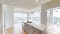 Located in the heart of downtown San Diego at 1150 E Street, this modern 2-bedroom, 2-bathroom residence offers a thoughtfully designed open-concept layout. The combined living, dining, and kitchen area serves as the centerpiece of the home, featuring light hardwood flooring, recessed lighting, and expansive floor-to-ceiling windows that flood the space with natural light and frame sweeping panoramic city views. The kitchen is anchored by a sleek island with a white quartz countertop, an undermount double sink, and contemporary gray cabinetry with black hardware. A private balcony extends the living space outdoors, offering additional views of the San Diego skyline. Both bedrooms continue the hardwood flooring and floor-to-ceiling window theme, providing generous natural light and impressive elevated city vistas. The bedrooms include mirrored sliding closet doors, maximizing both storage and the sense of space. The two bathrooms are finished with marble-style tile flooring and surrounds, gray vanity cabinetry, and clean white fixtures, delivering a polished, modern aesthetic. Additional conveniences include in-unit laundry and multiple closets throughout. The residence presents a bright, contemporary ambiance with a consistent neutral palette throughout.