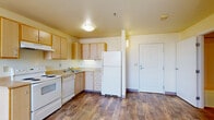 This efficiently designed one-bedroom, one-bathroom unit offers a thoughtful layout across a single floor, making smart use of every square foot. The kitchen is a functional highlight, featuring light maple cabinetry with ample storage, a full suite of white appliances including a range, dishwasher, and refrigerator, a single-basin sink, and durable hardwood-style flooring that extends into the entry area. Under-cabinet lighting and a ventilation hood add practical detail to the cooking space.

The open transition from the kitchen leads into a carpeted living area, which benefits from large windows that invite generous natural light and offer elevated views of the surrounding cityscape. A ceiling fan adds comfort to this airy space.

The bedroom is a quiet, carpeted retreat featuring a large window with continued outdoor views, a baseboard heater, and a sliding-door closet with built-in shelving and a hanging rod for organized storage.

The bathroom is clean and accessible, equipped with a vanity with light maple cabinetry, a large mirror, and safety grab bars, reflecting a thoughtful, accessibility-conscious design. Hardwood-style flooring carries through this space as well, tying the unit together with a cohesive aesthetic throughout.