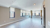 This contemporary urban residence is designed with a clean, modern aesthetic that maximizes natural light and open living. The spacious main living area is a standout feature, lined with a continuous band of large windows fitted with roller shades, offering expansive panoramic city views. Light hardwood-style flooring runs throughout, and an exposed concrete column adds an industrial character to the open layout.

The kitchen is thoughtfully designed with light wood-grain cabinetry extending from floor to ceiling, black matte hardware, a white vertical tile backsplash, warm-toned countertops, and a full suite of stainless steel appliances including a range, refrigerator, dishwasher, and built-in microwave. The kitchen flows seamlessly into the open living and dining area, making the space well-suited for both daily living and entertaining.

The residence includes a bedroom with a large window framing city views and the same consistent light flooring. Two bathrooms complete the layout: one featuring a tiled soaking tub and shower combination with matte black fixtures and wood-accented vanity, and a second with a glass-enclosed tiled shower stall and large-format tile flooring. Both bathrooms maintain a cohesive neutral palette with matte black hardware accents throughout.