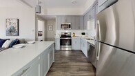 Located at 3 Marys Way in Lincoln, Massachusetts, this thoughtfully designed single-floor residence offers a contemporary living experience with clean lines and a neutral, light-toned palette throughout. The open living area is anchored by large black-framed windows that usher in generous natural light, creating an airy and welcoming atmosphere. Wood-look flooring runs through the main living spaces, adding warmth and visual continuity.

The kitchen is a standout feature, outfitted with sleek gray shaker-style cabinetry, white quartz countertops, a classic subway tile backsplash, and a full suite of stainless steel appliances including a refrigerator, range, microwave, and dishwasher. A kitchen island provides additional prep space and casual dining potential.

The bedrooms are carpeted for comfort, with neutral walls and ample natural light from well-placed windows. The primary bedroom benefits from a pair of windows with outdoor views. Additional bedrooms offer cozy, well-proportioned spaces with practical storage access.

Two bathrooms serve the residence: one features a soaking tub and shower combination with tile surround, while the second offers a walk-in tile shower. Both are finished with wood-toned vanities, undermount sinks, and large-format tile flooring, delivering a clean and modern aesthetic throughout.