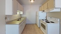 Located at 4265 Galley Rd in Colorado Springs, Colorado, this single-floor unit offers a straightforward and practical layout designed for efficient everyday living. The living area is finished with neutral-toned carpet and features a textured ceiling, large windows with vertical blinds that allow natural light to fill the space, and a baseboard heating system. The open feel of the main living area is complemented by a wet bar or kitchenette with upper cabinetry and a sink, providing added convenience. The galley-style kitchen is efficiently arranged with ample upper and lower cabinetry, a double-basin sink, tile flooring, and white appliances including a refrigerator and electric range. A dedicated bathroom includes a tiled tub-and-shower combination, toilet, and tile flooring, accessible directly from the main hallway. The bedroom is a well-proportioned, carpeted room with a window offering views of surrounding greenery and a baseboard heater. Throughout the unit, the neutral color palette and clean lines create a simple, functional ambiance suited to comfortable everyday living in the Colorado Springs area.