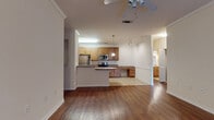This single-floor residence offers a thoughtfully designed open-concept layout that seamlessly connects the living area and kitchen. Rich hardwood-style flooring flows throughout the main living spaces, complemented by crown molding and ceiling fans that add a touch of classic detail. The kitchen is well-equipped with stainless steel appliances — including a refrigerator, electric range, and over-the-range microwave — paired with warm wood cabinetry and granite-style countertops. A curved peninsula provides additional prep and casual dining space, while tile flooring in the kitchen area adds a practical contrast to the rest of the home. Adjacent to the kitchen, a built-in desk area offers a convenient workspace. The living room is bright and open, with access to an exterior door and a dedicated in-unit laundry closet housing a full-size washer and dryer. The bedrooms are carpeted for comfort, each featuring a ceiling fan and natural light from windows with blinds. The bathroom is finished with tile flooring, a granite-style vanity, wood cabinetry, and a full tub-shower combination with tiled surround. Overall, the space presents a clean, functional, and comfortable living environment with consistent finishes throughout.