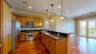 This thoughtfully designed 2-bedroom, 2-bathroom single-floor residence offers a comfortable and refined living experience across a well-utilized floor plan. The open-concept kitchen serves as a central highlight, featuring warm honey-toned cabinetry, dark granite countertops, a tile backsplash, stainless steel appliances, and a large center island with a built-in sink and pendant lighting overhead. Rich hardwood flooring flows throughout the kitchen and living areas, adding warmth and continuity to the space. Crown molding is present throughout, lending an elegant architectural finish. The living room is bright and airy, with French doors that open to a private balcony offering scenic outdoor views and generous natural light. Both bedrooms are carpeted for comfort, with the spacious primary bedroom benefiting from large windows and a ceiling fan. The primary bathroom features a tiled walk-in shower with glass doors, a wood vanity with a marble-style countertop, and tile flooring. The second bathroom includes a double-sink vanity with a marble-style countertop and a soaking tub with tile surround. Three closets provide ample storage throughout the residence, complementing the functional hallway that connects the living spaces seamlessly.