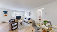 This single-floor residence is designed with a clean, contemporary aesthetic, characterized by white walls, light hardwood flooring in the main living areas, and an abundance of natural light streaming through large windows. The open-concept layout seamlessly connects the living room and dining area, creating a welcoming and functional shared space. The living room accommodates generous seating and features a large window overlooking greenery, while the adjacent dining area includes a round glass-top table, enhancing the sense of openness.

The kitchen is efficiently laid out with white shaker-style cabinetry, white countertops, and stainless steel appliances, including a gas range, built-in microwave, and dishwasher. Light hardwood flooring extends through this space, maintaining visual continuity throughout the unit.

The bedroom is a comfortable retreat with plush carpeting, natural light from a large window, and multiple closets providing ample storage. The full bathroom features neutral tile flooring, a white vanity, and a tiled shower surround, offering a clean and functional design.

A dedicated in-unit laundry area houses a full-size washer and dryer, adding significant everyday convenience. Overall, the space presents a bright, modern, and practical layout.