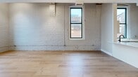 Located at 425 W Lakeside Ave in Cleveland, OH, this one-bedroom, one-bathroom loft showcases a compelling blend of historic industrial character and modern finishes. The open-concept kitchen and living area serves as the heart of the unit, where whitewashed exposed brick walls meet striking wood beam ceilings—a hallmark of the building's original construction. Light hardwood flooring runs throughout, enhancing the bright, airy atmosphere created by multiple black-framed windows that frame urban city views.

The kitchen is thoughtfully designed with white shaker-style cabinetry, white quartz countertops, a subway tile backsplash, and stainless steel appliances including a dishwasher and range. An in-unit LG washer is seamlessly integrated beneath the countertop for added convenience.

The bedroom offers a comfortable, well-proportioned layout with dual windows that allow natural light and city views to fill the space. Two closets provide ample storage throughout the unit.

The bathroom features clean, modern finishes including a white vanity with black hardware accents, a framed mirror, and hardwood-style flooring that ties the space together cohesively. A hallway connects the main living areas, completing this well-appointed urban loft.