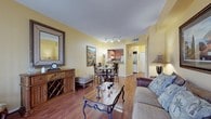 This single-floor residence offers a cohesive layout connecting its primary living spaces through an open, flowing design. The living room is finished with rich hardwood flooring and warm yellow walls, receiving generous natural light through large sliding glass doors that open to an outdoor area. A dining nook positioned adjacent to the living space is illuminated by track lighting overhead, creating a well-defined area for meals without sacrificing the open feel of the floor plan.

The kitchen is positioned just off the dining area and features a pass-through window that maintains visual connectivity with the living spaces. It is equipped with white cabinetry, granite-style countertops, stainless steel appliances including a dishwasher and range, and a double basin sink. Decorative fruit-themed border detailing adds a charming, personalized touch near the ceiling. An in-unit laundry area is conveniently located nearby.

The bedroom stands out with its distinctive faux-finish walls in soft sage tones, lending an elevated, textured aesthetic. Carpeted flooring adds warmth, and a window allows natural light to filter in. The en-suite bathroom offers a dual-sink vanity with ample counter space, a soaking tub with shower, and white tile flooring, completing this comfortable and characterful residence.