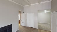 This single-floor residence showcases a thoughtfully arranged layout with a variety of distinct spaces connected through open archways and interior doorways. The living area immediately impresses with its striking vaulted ceilings accented by exposed beams, lending a sense of height and architectural character to the space. Neutral gray walls and plush carpeting create a calm, cohesive atmosphere throughout. A dark-tiled wood-burning fireplace serves as a focal point on one wall of the living room, while a sliding glass door fitted with vertical blinds invites natural light and provides access to an outdoor area.

Adjacent to the living space, the galley-style kitchen features rich, warm-toned wood cabinetry lining both sides, complemented by a double-basin sink, light countertops, and wood-look flooring. White appliances including a range and refrigerator complete the functional setup.

The hallway area transitions between the main living space and additional rooms, maintaining the same vaulted ceiling design with beamed detailing overhead. Carpeted bedrooms are generously sized with neutral walls, standard lighting fixtures, and multiple outlets. The 3D floor plan overview reveals a well-organized, interconnected layout that maximizes the available space efficiently across the single floor.