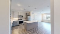 Located in Spring, TX, this well-designed 2-bedroom, 2-bathroom single-story residence offers a thoughtful layout with modern finishes throughout. The open-concept kitchen and living area serves as the heart of the home, featuring light wood-look flooring, recessed lighting, and a central island with a crisp white quartz countertop. The kitchen is equipped with stainless steel appliances, two-tone gray and light wood cabinetry, a subway tile backsplash, and pendant lighting, creating a clean, contemporary aesthetic. The living area flows seamlessly from the kitchen and benefits from abundant natural light through large windows with outdoor views. Both bedrooms feature ceiling fans, wide windows overlooking the outdoors, and wood-look flooring. The generously sized primary bedroom connects to a well-appointed en-suite bathroom showcasing marble-look tile flooring, a dual-sink vanity with gray cabinetry and black matte hardware, a large framed mirror, and a glass-enclosed walk-in shower. A spacious walk-in closet with dual hanging rods provides ample storage. The secondary bathroom offers a tiled tub-shower combination with matte black fixtures and open shelving. Two closets provide additional storage throughout the home.