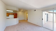 This single-story residence offers a well-organized layout with distinct living, kitchen, dining, and bedroom areas. The living room serves as a central gathering space, highlighted by a tile-surround fireplace with a classic white mantel flanked by two windows dressed in vertical blinds. Sliding glass doors on one wall bathe the room in natural light and provide access to an outdoor area with views of surrounding greenery. Soft, neutral carpeting runs throughout the living and bedroom spaces, contributing to a clean and cohesive aesthetic.

The kitchen is well-appointed with warm honey-toned wood cabinetry providing ample storage, white countertops, and white appliances including a gas range and over-the-range microwave. A skylight overhead fills the space with natural light, while wood-look flooring adds a practical and attractive finish. A curved pass-through bar connects the kitchen to the adjacent living and dining area, promoting an open, communicative flow between spaces.

The bedrooms are generously proportioned, featuring vaulted ceilings that enhance the sense of space, carpet flooring, and sliding glass door access in at least one room. The bathroom includes a full tub-shower combination with white tile surround and wood-look tile flooring, maintaining the residence's consistently clean and neutral palette throughout.