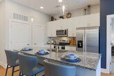 Located at 2–14 S Clayton St in Lawrenceville, GA, this thoughtfully designed single-floor residence offers a cohesive blend of modern finishes and functional living spaces. The open kitchen is a standout feature, showcasing granite countertops, white shaker cabinetry extending to the ceiling, stainless steel appliances including a range, microwave, and refrigerator, and a peninsula with bar seating — all set atop warm wood-look flooring. The living area is bright and welcoming, with large sliding glass doors leading to a private balcony that frames outdoor views, complemented by a bold accent wall and stylish décor. Multiple bedrooms provide comfortable retreats, each featuring plush carpeting, generous windows with natural light, and ample space. The primary bedroom connects to a well-appointed en-suite bathroom with granite countertops, white cabinetry, brushed nickel fixtures, a framed mirror, and a glass-enclosed walk-in shower. A second bathroom mirrors the same quality finishes. Throughout the residence, a consistent neutral palette punctuated by contemporary accents creates a polished and inviting atmosphere well-suited for modern living in the heart of Lawrenceville.