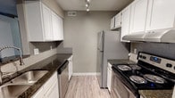 This upgraded 2-bedroom, 2-bathroom residence offers a thoughtfully designed single-floor layout with contemporary finishes throughout. The open living area is a standout, featuring rich wood-look plank flooring, neutral gray walls, and a tiled fireplace that serves as a focal point. Large windows and a glass patio door allow generous natural light to fill the space, creating a bright and welcoming ambiance.

The galley-style kitchen is well-appointed with white shaker cabinetry, dark granite countertops, a gray subway tile backsplash, and stainless steel appliances including a refrigerator, dishwasher, and electric range. Light luxury vinyl flooring and track lighting complete the polished look. A pass-through opening connects the kitchen to the main living area, enhancing the sense of flow.

Both bedrooms are comfortably sized, featuring plush carpeting, warm taupe walls, and windows with outdoor views that bring in natural light. Each bathroom reflects the same upgraded aesthetic, with dark granite vanity countertops and clean white fixtures. One bathroom includes a full tub/shower combination with a safety grab bar, while the second features a spacious vanity with a mirror. Overall, the space presents a clean, modern, and move-in-ready environment.