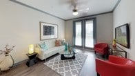 This single-floor residence offers a thoughtfully designed layout with modern finishes throughout. The kitchen serves as a central highlight, featuring white cabinetry, a teal glass tile backsplash, granite countertops, and a suite of stainless steel appliances including a range, over-the-range microwave, and French door refrigerator. A spacious island with bar seating and pendant lighting overhead makes it ideal for both cooking and casual dining. Hardwood-style flooring runs through the kitchen and living areas, adding warmth and continuity.

The living area is bright and welcoming, with large double doors that invite natural light and provide outdoor access. Crown molding, a ceiling fan, and neutral walls create a polished yet comfortable atmosphere.

The bedroom is a calm retreat finished with plush carpeting, large windows, and direct access to a private outdoor space. A decorative wall accent above the bed adds a refined touch, while dual nightstands and lamps provide functional symmetry.

The bathroom features wood-style flooring, a granite-topped vanity with a vessel sink, a large mirror, and a full tub-shower combination, all finished in a clean, contemporary palette. A dedicated media nook with wall-mounted TV and seating rounds out this well-organized residence.