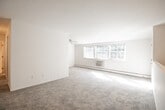 Located at 1998 NY-112 S in Coram, New York, this single-floor unit offers a well-organized layout designed for comfortable everyday living. The open living area is finished with plush wall-to-wall carpeting and features a ceiling fan, a baseboard heating unit, and a wall-mounted air conditioning unit. Large windows allow natural light to fill the space, creating a bright and airy atmosphere throughout.

The bedroom is generously proportioned, also finished with soft carpeting, and benefits from abundant natural light. It includes multiple closets — an open shelving closet and two additional sliding-door closets — providing exceptional storage capacity. A second carpeted room with its own closet offers flexibility as an additional bedroom or home office.

The kitchen is equipped with warm oak cabinetry, light laminate countertops, a stainless steel single-basin sink, and stainless steel appliances including a gas range and an over-the-range microwave. Tile flooring completes the kitchen's clean, functional look.

The full bathroom features white tile flooring, a single-sink vanity with a mirrored medicine cabinet, a toilet, and a tub-and-shower combination enclosed by sliding glass doors. The overall aesthetic throughout the unit is neutral and move-in ready, with white walls and light tones creating a clean, cohesive environment.