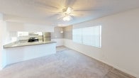 This single-floor residence offers a well-organized layout designed for comfortable everyday living. The open-concept living and dining area serves as the heart of the space, featuring plush carpeted flooring, a ceiling fan with integrated lighting, and a large window fitted with vertical blinds that invite abundant natural light throughout the day. The kitchen is thoughtfully designed with white cabinetry, light-toned countertops, wood-look flooring, a stainless steel refrigerator, and a recessed skylight-style ceiling feature that brightens the workspace. A peninsula counter provides a natural transition between the kitchen and the adjoining living area, making the space feel connected and functional. The bedrooms are carpeted and bright, each equipped with ceiling fans and access to natural light through sizable windows with vertical blinds. Closet storage is built in, with at least one bedroom featuring a dedicated closet with bifold doors. The bathroom is clean and efficiently laid out, offering a full tub and shower combination with chrome fixtures, complemented by wood-look tile flooring. Throughout the space, textured ceilings and a neutral color palette create a cohesive, understated aesthetic that provides a versatile backdrop for personalization.