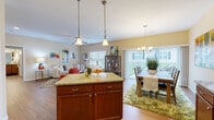 This single-floor, 2-bedroom, 2-bathroom home offers a thoughtfully designed open-concept layout that seamlessly connects the kitchen, dining, and living areas. The kitchen is a functional centerpiece, featuring rich wood cabinetry, granite countertops, a full suite of stainless steel appliances, and a central island with bar seating — ideal for casual dining or entertaining. Pendant lighting above the island and recessed ceiling lights add layered illumination throughout.

The dining area sits adjacent to the kitchen and is bathed in natural light from a large sliding glass door fitted with vertical blinds, providing outdoor access. A stylish chandelier anchors the space above. The living room continues the warm hardwood flooring found throughout the main areas, complemented by a ceiling fan, bright windows, and generous wall space.

Both bedrooms feature plush carpeting and neutral walls that create a calm, restful atmosphere. The spacious primary bedroom offers ample room for a king-size bed. The bathrooms are finished with wood-toned cabinetry, granite vanity tops, and hardwood-style flooring. A dedicated closet adds practical storage to the layout. Overall, the home presents a cohesive, warm aesthetic with consistent finishes throughout.