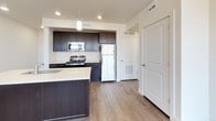 This single-floor residence offers a clean, modern aesthetic defined by neutral tones, wood-look flooring, and an efficient, well-organized layout. The kitchen is a standout feature, equipped with dark espresso cabinetry, light quartz countertops, a subway tile backsplash, stainless steel appliances including a gas range, microwave, and refrigerator, and a peninsula island with pendant lighting overhead. Recessed lighting and a direct entry corridor make the kitchen area feel polished and functional. The living and dining areas are open and airy, with large windows and a sliding glass door that invites generous natural light and outdoor views. A chandelier adds a touch of elegance to the dining space. The bedrooms are carpeted for comfort and feature windows on multiple walls, offering panoramic views of the surrounding area. One bedroom includes a ceiling fan for added comfort. The primary bathroom connects to a walk-in closet and features a glass-enclosed shower, wood-look tile flooring, and dark vanity cabinetry. A secondary bathroom offers a full tub-shower combination, toilet, and matching vanity. Throughout, the space maintains a consistent, contemporary finish with white trim and a bright, welcoming atmosphere.