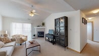 This single-floor residence offers a thoughtfully arranged layout that balances comfort and functionality. The living room serves as the heart of the home, distinguished by vaulted ceilings that lend a sense of openness and volume to the space. A ceiling fan provides both style and practicality, while large vertical-blind windows allow generous natural light to fill the room. A white-mantled fireplace anchors one wall, adding warmth and a classic focal point to the living area, which is finished with neutral carpet throughout.

The kitchen features ample white cabinetry with wood trim detailing, white appliances including a refrigerator, range, and dishwasher, and light tile flooring. An adjacent dining area accommodates a round table, making it well-suited for everyday meals.

The bedroom is a calm, carpeted retreat with a ceiling fan, vertical-blind window, and a closet with natural wood doors. Two full bathrooms serve the home; one includes a double-sink vanity with wood-trimmed cabinetry and a shower-tub combination, while the second offers a similar tub-shower setup with a single-sink vanity and tile flooring. Throughout the home, neutral tones and clean finishes create a bright, welcoming ambiance.