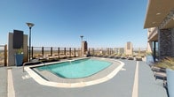 Located at 2610 N Houston Street in Dallas, Texas, this rooftop amenity level offers a well-appointed outdoor retreat with commanding views of the Dallas skyline. The centerpiece of the space is a generously sized resort-style swimming pool with a smooth tile surround, flanked by rows of lounge chairs ideal for sunbathing under the Texas sky. A full-length glass railing system lines the perimeter, preserving panoramic city views while providing an open, airy atmosphere.

Adjacent to the pool, a covered lounge area provides a shaded retreat furnished with comfortable wicker sectional sofas accented by teal and patterned throw pillows. This sheltered zone features recessed ceiling speakers and direct access to the pool deck, creating a seamless indoor-outdoor flow. A dedicated outdoor entertainment wall showcases a stacked stone tile facade, a sleek gas fireplace with a stainless steel surround, and a wall-mounted flat-screen television above—an ideal gathering spot for social events.

A separate sun-drenched lounge nook features floor-to-ceiling glass sliding doors that frame sweeping views of the surrounding cityscape, flooding the space with abundant natural light. The overall design of the amenity level balances modern urban aesthetics with relaxed, resort-inspired comfort throughout.