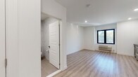 This thoughtfully renovated single-floor unit showcases a clean, contemporary design with consistent light wood-tone flooring and crisp white walls throughout, creating a bright and cohesive aesthetic.

The kitchen is a standout feature, outfitted with two-tone cabinetry — dark charcoal lower cabinets paired with white upper cabinets — all accented with brushed gold hardware. Black countertops, a matte black farmhouse sink, a mosaic tile backsplash, and a full suite of stainless steel appliances, including a range, microwave, dishwasher, and refrigerator, complete this functional and stylish space. A louvered closet door and recessed lighting add practical and polished touches.

The living area is open and airy, benefiting from a large black-framed window that invites natural light and outdoor views. A wall-mounted HVAC unit ensures year-round comfort.

The bathroom is elegantly finished with floor-to-ceiling marble-look tile, a deep soaking tub with a glass enclosure and rainfall showerhead, a dark vanity with a black countertop and gold hardware, a mirrored medicine cabinet, and large-format floor tiles. Every detail reflects a high standard of modern design, making this a well-appointed and move-in-ready space.