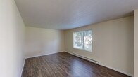 Located at 11721 E Nora Ave in Spokane Valley, WA, this two-bedroom, one-bathroom unit offers a thoughtfully arranged single-floor layout. Dark hardwood-style flooring flows throughout the main living areas and hallway, adding warmth and visual continuity. The living room is bright and inviting, featuring a large window that frames views of mature trees and greenery, complemented by a baseboard heating system and a textured ceiling. The kitchen is efficiently designed with warm wood cabinetry, laminate countertops, a double-basin sink, and a dishwasher, providing ample functionality for everyday use. The hallway connects the living spaces to the two bedrooms, each featuring neutral walls and dedicated closet space. The primary bedroom offers a generous footprint, while the second bedroom is finished with soft carpeting. The full bathroom includes a tub-shower combination with accessibility grab bars and hardwood-style flooring. A private patio extends the living space outdoors. The surrounding community grounds showcase expansive, well-manicured lawns, large shade trees, and a playground area, creating a serene and family-friendly environment.
