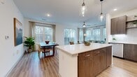 Located at 9821 Research Drive in Charlotte, NC, this well-appointed three-bedroom, three-bathroom residence offers a thoughtfully designed single-floor layout with modern finishes throughout. The open-concept living, dining, and kitchen area serves as the heart of the home, where large windows on multiple walls flood the space with natural light and frame serene, wooded views. A private balcony, accessible through sliding glass doors, extends the living area outdoors.

The kitchen is outfitted with rich walnut-toned cabinetry, quartz countertops, stainless steel appliances, and a central island with pendant lighting overhead — ideal for both cooking and casual entertaining. Wood-look flooring runs consistently throughout the unit, lending warmth and cohesion to every room.

The dining area benefits from its own window overlooking the tree line, creating a bright and pleasant setting. The living room features a ceiling fan and corner windows that maximize light and views.

Each bedroom offers a comfortable retreat, with the primary suite showcasing a bold teal accent wall, sconce lighting, walk-in closet, and an en-suite bathroom complete with dual vanity, quartz surfaces, walnut cabinetry, and a glass-enclosed shower. The overall ambiance is modern, warm, and serene.