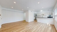This single-floor unit presents a clean, modern aesthetic defined by crisp white walls, warm light oak-toned hardwood-style flooring, and bright recessed lighting throughout. The entry hallway provides a welcoming transition into the home, with an intercom panel conveniently positioned near the front door. The open-concept living and dining area is generously proportioned, featuring a textured ceiling with recessed pot lights that create a well-lit, airy atmosphere. This space flows seamlessly into the kitchen, which is appointed with white shaker-style cabinetry, grey countertops, a classic white subway tile backsplash, stainless steel appliances including a refrigerator and electric range, and a double basin sink. A kitchen island with an overhang provides additional prep space and casual seating. The bedrooms are comfortably sized, each featuring sliding or hinged closets with built-in shelving and bright white walls. The bathroom is finished with full white subway tile surround, a soaking bathtub, a vanity with an integrated sink, and a window that brings in natural light. Throughout the unit, consistent flooring and neutral tones create a cohesive and move-in ready living environment.