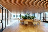 Located at 1070 Bridgeview Way in San Francisco's Mission Bay neighborhood, this thoughtfully designed single-floor space offers a refined blend of natural materials and modern architecture. The open-plan layout is anchored by a distinctive wood-slatted ceiling that runs throughout, adding warmth and acoustic depth while housing recessed and track lighting. Underfoot, light oak herringbone-patterned flooring lends an elegant, gallery-like quality to the entire space.

The centerpiece of the room is a large, oval wooden table surrounding a built-in live planter overflowing with lush tropical greenery, creating a biophilic focal point that brings nature indoors. Comfortable seating is arranged around the table, making it well-suited for collaborative meetings or casual gatherings.

Floor-to-ceiling windows line multiple walls, flooding the interior with abundant natural light and providing views of the surrounding San Francisco cityscape. Black-framed glass partition doors and walls add a contemporary industrial contrast to the warm wood tones. White walls display curated artwork, enhancing the creative atmosphere. A lounge area with accent seating is tucked near the windows, offering a quieter retreat within the space. The overall ambiance is sophisticated yet inviting, balancing functionality with a strong design sensibility.