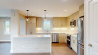Located at 550 Sheridan Square in Evanston, IL, this thoughtfully designed 3-bedroom, 2-bathroom residence offers a well-appointed single-floor layout with modern finishes throughout. The open-concept living room is a standout, featuring warm hardwood-style flooring, recessed lighting, and a bank of large windows alongside sliding glass doors that lead to a private balcony, filling the space with abundant natural light and views of the surrounding neighborhood. The kitchen is a true highlight, showcasing light wood cabinetry, white quartz countertops, a classic subway tile backsplash, and a full suite of stainless steel appliances including a double oven and dishwasher. Pendant lighting above the central island adds a refined touch. The spacious primary bedroom offers recessed lighting and a window with outdoor views. Additional bedrooms are finished with the same hardwood-style flooring and neutral tones, offering versatile use. The two bathrooms are elegantly appointed — one features a walk-in glass shower with floor-to-ceiling marble-style tile, penny-round mosaic flooring, and brushed gold fixtures, while the second includes a soaking tub with matching marble-style tile surround. Recessed lighting and hexagonal tile flooring complete the clean, contemporary aesthetic throughout.
