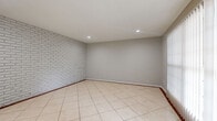 Located at 7637 Harwin Dr in Houston, TX, this single-story, 2-bedroom, 1-bathroom home offers a practical and cohesive layout throughout. Light-toned ceramic tile flooring runs consistently across all rooms, lending a clean, unified look to the entire space.

The living room serves as a standout area, featuring a white-painted brick accent wall and recessed lighting that adds character and a warm ambiance. Adjacent to the living area, the combined dining room is highlighted by an elegant chandelier and a built-in shelving nook, perfect for display or storage.

The galley-style kitchen is efficiently designed with granite-look countertops, ample white cabinetry, a mosaic tile backsplash, and stainless and black appliances including a refrigerator and electric range.

Both bedrooms are well-proportioned, with the primary bedroom offering a ceiling fan, a window for natural light, and access to a generous walk-in closet fitted with dual hanging rods and a central shelving unit. The full bathroom includes a wide vanity with granite-look countertops, white cabinetry, and a large mirror.

A hallway connects the main living areas to the bedrooms and bathroom, while a smart-lock front entry door opens into a welcoming foyer. The neutral gray walls throughout create a calm, move-in-ready atmosphere.