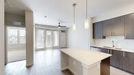 This well-appointed one-bedroom, one-bathroom residence in Rochester Hills, Michigan offers a thoughtfully designed open-concept layout with modern finishes throughout. The kitchen serves as a focal point of the living area, showcasing dark espresso cabinetry that extends to the ceiling for ample storage, a large quartz-topped center island with pendant lighting above, a crisp white tile backsplash, and a full suite of stainless steel appliances including a refrigerator, range, microwave, and dishwasher. Light wood-style flooring flows seamlessly from the kitchen into the living room, which is bathed in natural light from a wall of floor-to-ceiling glass doors fitted with blinds and equipped with a ceiling fan. The bedroom features plush carpeting, multiple windows that invite generous daylight and outdoor views, and a ceiling fan for added comfort. A dedicated closet provides practical storage. The bathroom is finished with a wide white quartz vanity countertop, a blue-toned modern cabinet base, a framed mirror, and stylish light fixtures, with durable wood-style flooring underfoot. Clean neutral walls and crisp white trim throughout lend the space a cohesive, contemporary aesthetic.