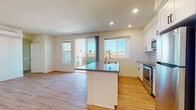 Located at 310-340 Palm Ave in National City, CA, this modern single-floor residence offers a clean, contemporary design with light wood-style flooring that flows seamlessly throughout every room. The open-concept layout connects the kitchen and living area, creating a spacious, functional environment ideal for everyday living. The kitchen is well-appointed with white shaker cabinetry extending to the ceiling, a white subway tile backsplash, a full suite of stainless steel appliances including a refrigerator, range, and microwave, and a peninsula with a dark countertop and integrated sink. Recessed lighting illuminates the space, while large sliding glass doors and multiple windows invite abundant natural light and provide views of the surrounding neighborhood. A wall-mounted mini-split unit serves the living area for efficient climate control. The bedrooms are bright and simply finished with neutral walls and windows that bring in daylight. The bathroom features a white vanity with dark hardware, a tiled tub-shower combination, and wood-style flooring that ties the space together. The overall ambiance is fresh, clean, and move-in ready, reflecting a modern residential aesthetic throughout.