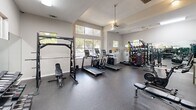 Located at 2941 Springsweet Lane in Raleigh, North Carolina, this dedicated fitness center offers a comprehensive exercise environment within a single, open-plan room. The space is finished with durable rubber flooring throughout, providing excellent traction and cushioning for a variety of workouts.

Natural light fills the room through multiple large windows fitted with horizontal blinds, offering views of the surrounding greenery and keeping the atmosphere bright and energizing. A ceiling fan and recessed lighting ensure consistent comfort and visibility regardless of the time of day.

The cardio zone is prominently featured and includes multiple treadmills and an elliptical machine, arranged to take full advantage of the natural light. A stationary spin bike with an integrated screen adds a modern interactive training option. Strength training is well represented with a cable machine system, a squat/power rack, a full dumbbell rack with an extensive range of weights, a weight bench, and a multi-station functional trainer. A punching bag rounds out the strength and conditioning offerings.

Full-length mirrors along one wall visually expand the space and support proper form during workouts. A wall-mounted flat-screen television provides entertainment or instructional content. The clean, neutral-toned walls and open layout create an organized and motivating environment suited for a wide range of fitness goals.