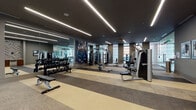Located on Raleigh Street in Denver's West Colfax neighborhood, this single-level fitness center is thoughtfully designed to accommodate a comprehensive range of workout needs. The space is organized into distinct functional zones, including a strength training area, a dedicated cycling studio, and a cardio zone, all connected by a spacious, open floor plan that promotes ease of movement throughout.

The interior design is contemporary and polished, featuring a dark ceiling with striking linear LED lighting that runs in parallel rows, creating a sleek, high-contrast aesthetic. Striped carpeting in neutral tones of beige and gray defines the floor throughout, contributing to the overall modern look while providing comfort underfoot. Full-length mirrors line portions of the walls, visually expanding the space and supporting proper form during exercise.

The strength training area is well-appointed with a comprehensive dumbbell rack, multiple cable machines, weight benches, and a functional trainer. The cardio zone features a row of elliptical machines and treadmills positioned near large floor-to-ceiling windows, offering natural light and outdoor views. The cycling studio includes stationary bikes, a large display screen, and mirrored walls. Motivational fitness artwork and framed prints are displayed throughout, enhancing the energetic atmosphere of the space.
