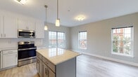 Located at 502 Howe Ave in Shelton, Connecticut, this thoughtfully designed single-floor residence offers a clean, modern aesthetic throughout. The open-concept kitchen and living area serves as the heart of the space, anchored by a large central island with a striking granite countertop. The kitchen is outfitted with crisp white shaker cabinetry, a classic subway tile backsplash, stainless steel appliances including a refrigerator, range, microwave, and dishwasher, and elegant pendant lighting that adds a warm, refined touch. Multiple windows allow natural light to pour into the combined kitchen and living area, offering views of the surrounding neighborhood. Light-toned hardwood-style flooring runs seamlessly throughout the entire unit, enhancing the bright and airy atmosphere. The bedroom is a well-proportioned, tranquil retreat with a dedicated closet and continued access to natural light through a generously sized window. The bathroom features marble-style tile flooring, a full soaking tub and shower combination, a gray vanity with integrated sink, and a window for added ventilation. Clean white panel doors and soft neutral wall tones contribute to the cohesive, contemporary feel of the entire space.