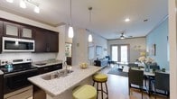 This 2-bedroom, 2-bathroom residence in the White Oak community is designed with an open-concept floor plan that seamlessly connects the kitchen, dining, and living areas. The kitchen serves as a central hub of the home, featuring dark espresso cabinetry, a white subway tile backsplash, and a granite-topped island with built-in sink. Pendant lighting hangs above the island, which also provides casual seating with bar-height stools. Recessed lighting and crown molding add refined detail to the ceilings throughout.

The living area is generously proportioned, with light-toned flooring, a ceiling fan, and French doors that allow natural light to fill the space while offering access to the outdoors. The open sightlines between the kitchen and living room create an airy, connected ambiance well-suited for both everyday living and entertaining. The neutral color palette throughout provides a clean, versatile backdrop. Together, the functional layout, quality finishes, and abundant natural light make this a well-appointed and comfortable single-story home.