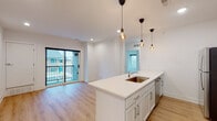 This thoughtfully designed single-floor residence offers a bright, contemporary living experience with a cohesive open layout and high-quality finishes throughout. The heart of the unit is a well-appointed kitchen anchored by a large center island with a sleek white quartz countertop and an undermount sink. White shaker cabinetry provides ample storage, while stainless steel appliances — including a refrigerator, electric range, and over-the-range microwave — complete the modern look. Stylish pendant globe lights hang above the island, adding a warm, inviting glow. The kitchen flows seamlessly into the living area, which opens to a private balcony through sliding glass doors, bringing in natural light and outdoor views. Light-toned hardwood flooring runs throughout the entire unit, enhancing the sense of openness and continuity. The bedrooms are generously sized, each featuring multiple windows that frame views of surrounding greenery and include ceiling fans for added comfort. The bathrooms are finished in a clean, minimalist style — one offering a full soaking tub and shower combo with white cabinetry, and another featuring a single vanity with a large picture window. The overall ambiance is modern, bright, and move-in ready.