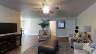 This two-story home offers a thoughtfully designed layout that balances comfort and functionality. The main level centers around a spacious open-concept living area, where hardwood-style flooring flows seamlessly underfoot, complemented by neutral-toned walls that create a bright and welcoming atmosphere. A ceiling fan with integrated lighting anchors the living room, providing both air circulation and ambient illumination. The generous living space comfortably accommodates multiple seating arrangements, making it well-suited for relaxing or entertaining. A staircase with white railings leads to the upper floor, adding a classic architectural touch to the main level. The entry area features a framed window that allows natural light to filter in, enhancing the openness of the space. A textured ceiling adds subtle visual depth throughout. The open sightlines between the living area and adjacent spaces, including a glimpsed dining or kitchen area, reinforce the home's connected and airy feel. The second floor provides additional living or sleeping quarters, expanding the overall capacity of the home. Clean white doors, consistent trim work, and cohesive finishes throughout reflect a polished, move-in-ready interior.