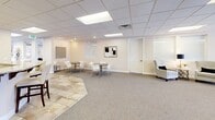 Located at 14527 S Travel Dr in Draper, Utah, this single-floor commercial space offers a well-appointed, open-concept layout designed for both comfort and functionality. The interior is finished with a drop-tile ceiling fitted with recessed panel lighting, and a combination of plush carpeting and stone tile flooring that defines distinct activity zones throughout.

A standout feature of the space is the floor-to-ceiling stone tile fireplace surround, which anchors the lounge area and adds a warm, upscale ambiance. Adjacent to the fireplace, a seating arrangement with leather sofas and accent chairs creates an inviting gathering space. A row of windows along one wall frames views of the surrounding Draper landscape, filling the area with natural light.

Toward the entry, a bar-height counter with dark cabinetry and barstools provides a casual seating option. Dual glass-panel doors with sidelights create a polished, professional entry point. Additional areas within the space accommodate small dining or meeting tables with modern chairs, offering flexible configurations for various uses.

Curated wall art and decorative accents are distributed throughout, contributing to a refined yet approachable aesthetic. A private room with a glass partition is also present, suitable for meetings or focused work. Overall, this space combines a contemporary design sensibility with practical versatility.