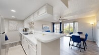 This single-floor unit offers a thoughtfully designed layout that maximizes its compact footprint across four distinct spaces. The open-concept kitchen and living room serve as the heart of the unit, where a galley-style kitchen features white cabinetry, white quartz countertops, a peninsula with bar seating, and ample upper and lower storage. The kitchen flows seamlessly into the living and dining area, which is anchored by a ceiling fan and bathed in natural light from large sliding glass doors that open to an outdoor space, offering views of surrounding greenery. The dedicated office provides a quiet, functional workspace complete with its own ceiling fan, a window with natural light, and enough room for a full desk setup. The bathroom is finished with white cabinetry, a quartz vanity surface, and a tub-shower combination. Throughout the unit, light wood-style flooring creates a cohesive and modern aesthetic, while textured ceilings add a classic touch. The consistent use of white tones in the kitchen and bathroom, paired with neutral walls, gives the entire space a clean, bright, and inviting character that makes it feel open and airy.