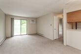 This single-floor residence offers a practical and comfortable layout with well-defined living spaces throughout. The living room is generously sized, featuring soft wall-to-wall carpeting, warm beige walls, and a textured ceiling. A sliding glass door fills the room with natural light and provides direct access to a private balcony overlooking a green outdoor setting. A wall-mounted air conditioning unit and baseboard heating ensure year-round comfort. The living area connects seamlessly to a dining space highlighted by a ceiling fan and a pass-through opening to the kitchen, framed by warm wood cabinetry above.

The kitchen is efficiently arranged in a galley style, featuring oak-toned cabinetry, white countertops, a stainless steel sink, tile flooring, and white appliances including an electric range and over-the-range microwave. The bedroom is carpeted and bright, with a window offering pleasant views of the surrounding greenery, a ceiling fan, and baseboard heating for comfort. The full bathroom is cleanly appointed with a single-sink vanity topped with a mirrored medicine cabinet, tile flooring, a toilet, and a full-size tub and shower combination. Overall, this unit presents a cohesive, functional living environment with consistent warm neutral finishes and ample natural light.