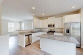 Located at 2001 Wood Hollow Place in Frederick, MD, this three-story home offers four bedrooms and four bathrooms spread across three well-proportioned floors. The entry level features a welcoming hallway with light hardwood flooring, carpeted stairs with a clean white rail, and access to the utility room, which includes sliding glass doors opening to the outdoors. The main living floor centers around an open-concept kitchen and living room. The kitchen is outfitted with white shaker-style cabinetry, granite countertops, stainless steel appliances including a gas range, built-in microwave, dishwasher, and refrigerator, all set on light hardwood floors. The upper floors house the four bedrooms, each featuring natural light from windows with blinds. Flooring varies between light hardwood and plush carpet depending on the room. The bathrooms are finished with white vanities, solid-surface countertops, large mirrors, and chrome fixtures. A dedicated laundry room with a full-size washer and dryer adds everyday convenience. The home's neutral palette, recessed lighting, and consistent finishes throughout create a clean, modern ambiance well-suited to a variety of living arrangements.